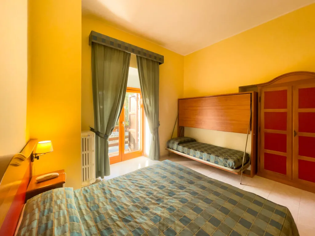 camera con letto matrimoniale, letto singolo accanto alla finestra con tende verdi e pareti gialle